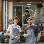 Positive man with cup of coffee and woman with filter holder standing on terrace of modern cafe during work break